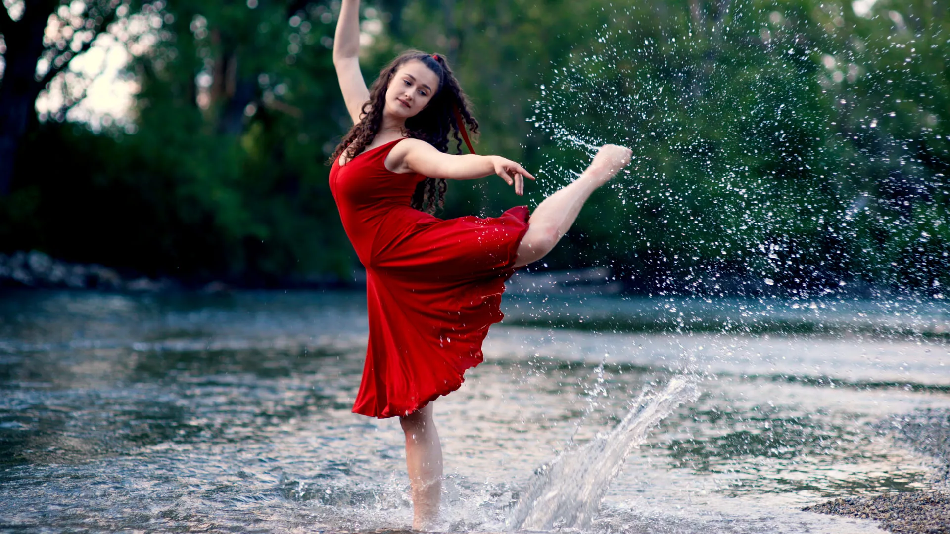 Tänzerin im roten Kleid springt im Wasser, Wassertropfen spritzen auf