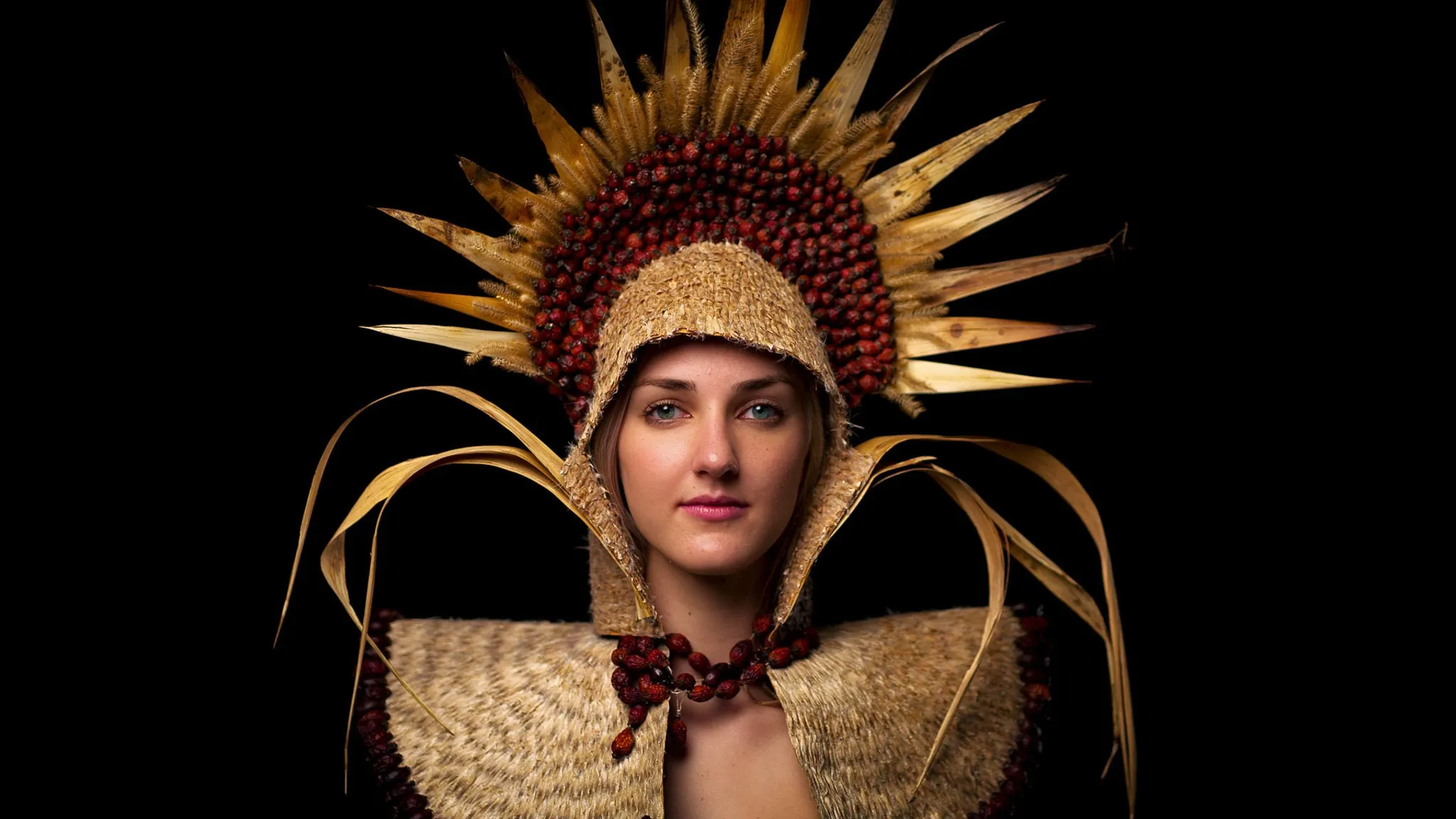 Frau mit ausladendem goldenem Kopfschmuck aus Naturmaterialien vor schwarzem Hintergrund