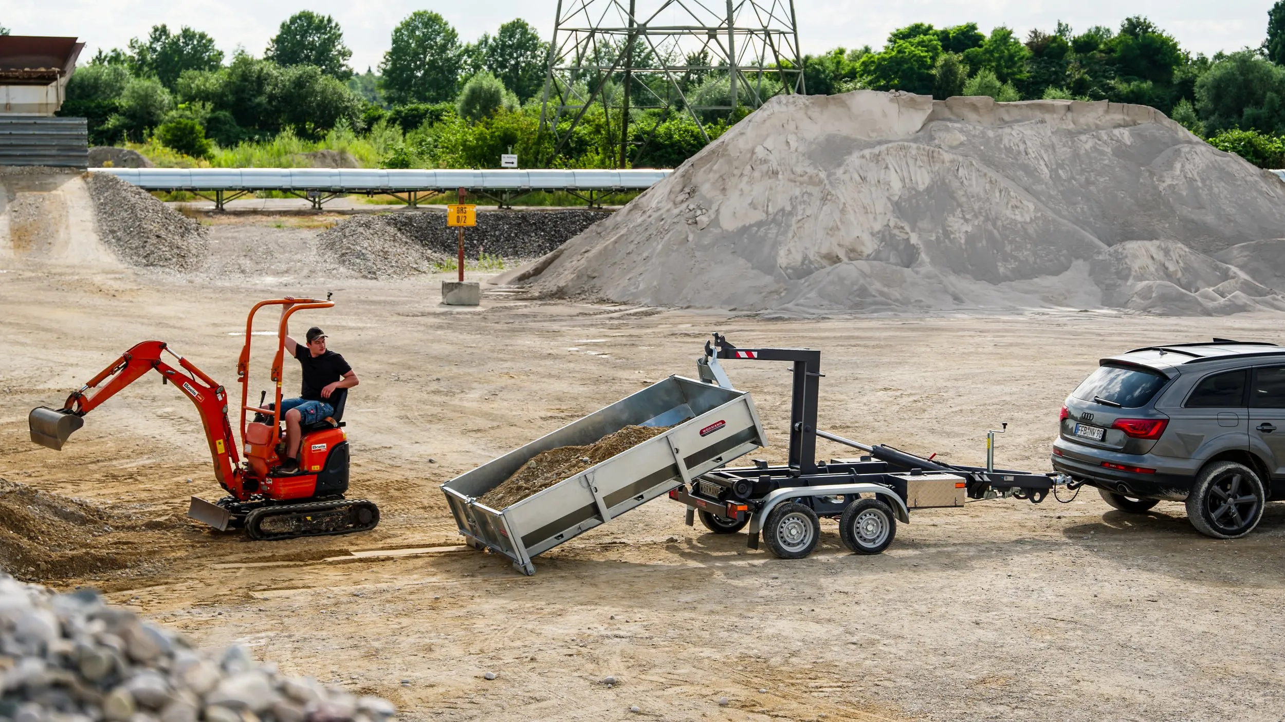 Minibagger und Anhänger mit Container auf dem Kiesgelände