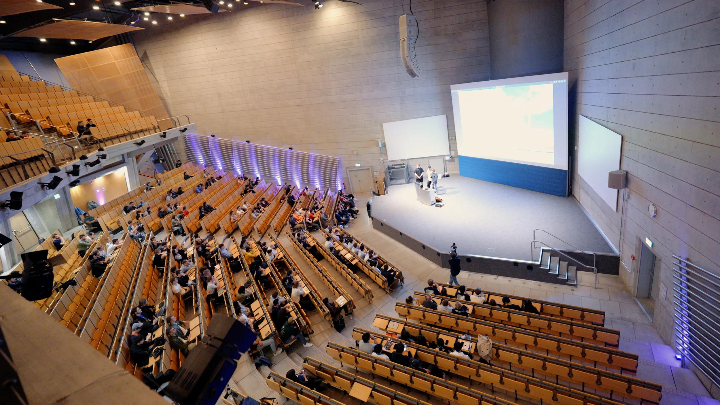 Blick von oben in einen gut besetzten Hörsaal mit Leinwand