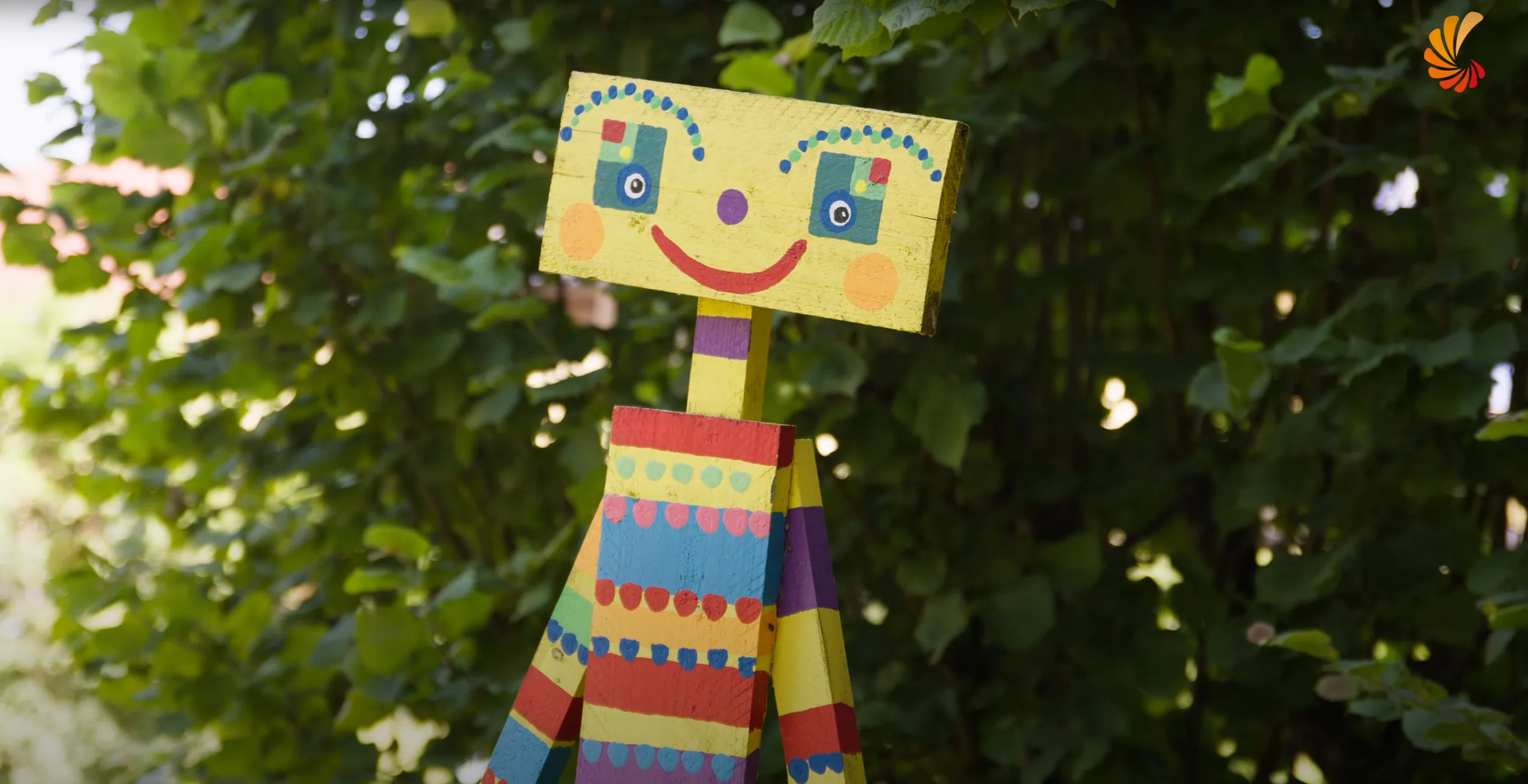 Bunt bemalte Figur aus Pappe vor grünen Blättern