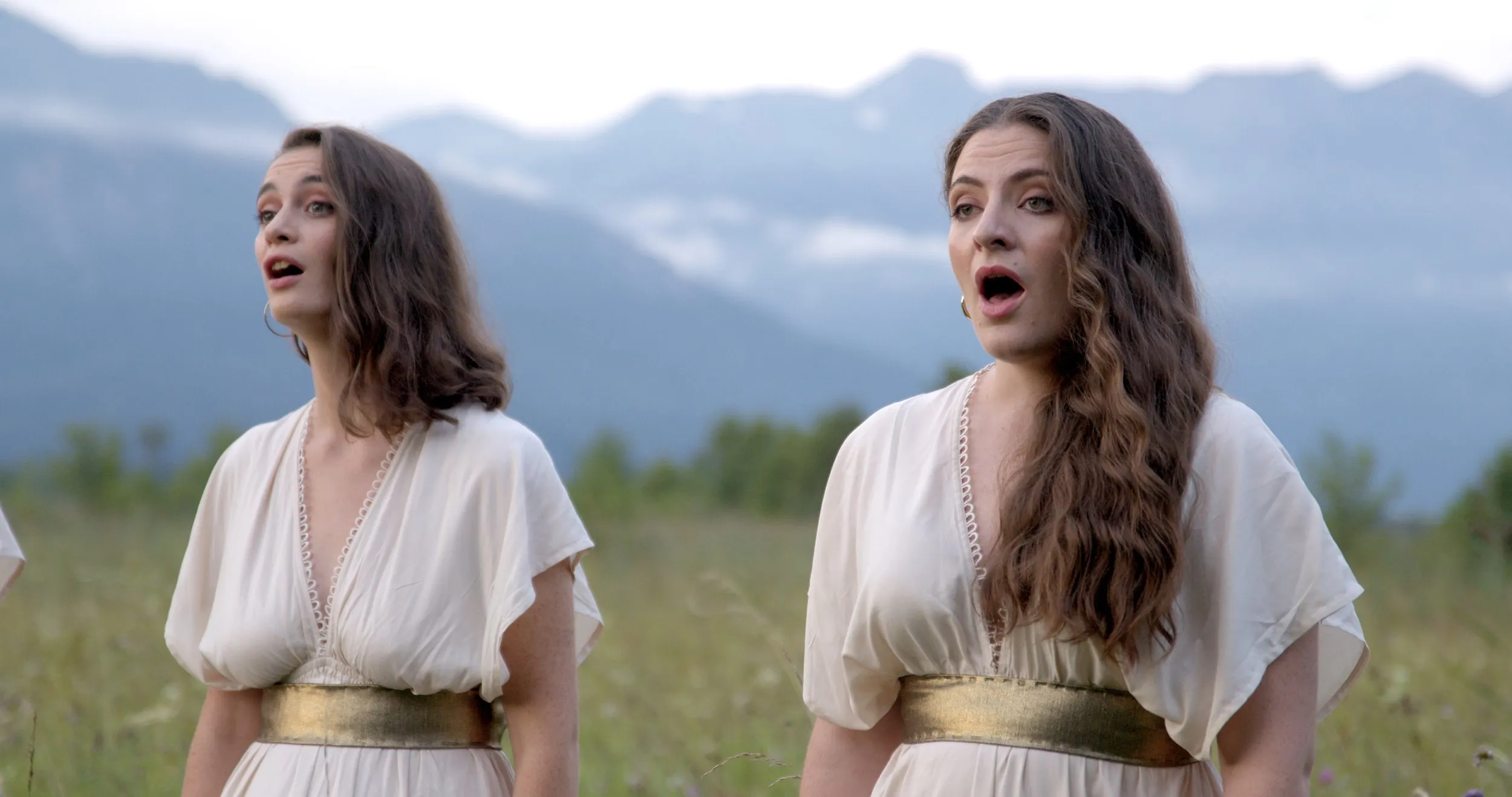 Zwei Sängerinnen in weißen Kleidern singen vor Bergpanorama