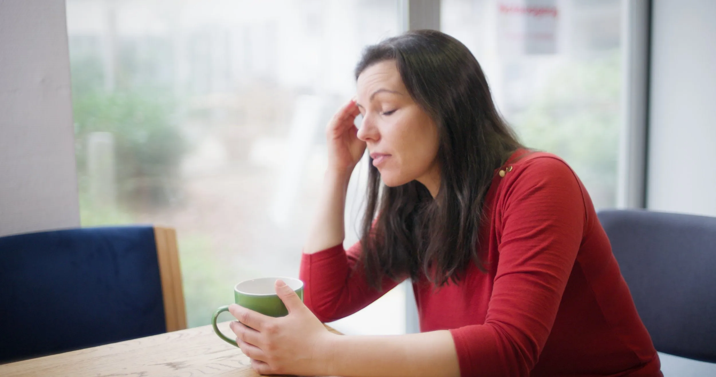 Frau sitzt nachdenklich mit einer Tasse am Tisch und stützt den Kopf auf