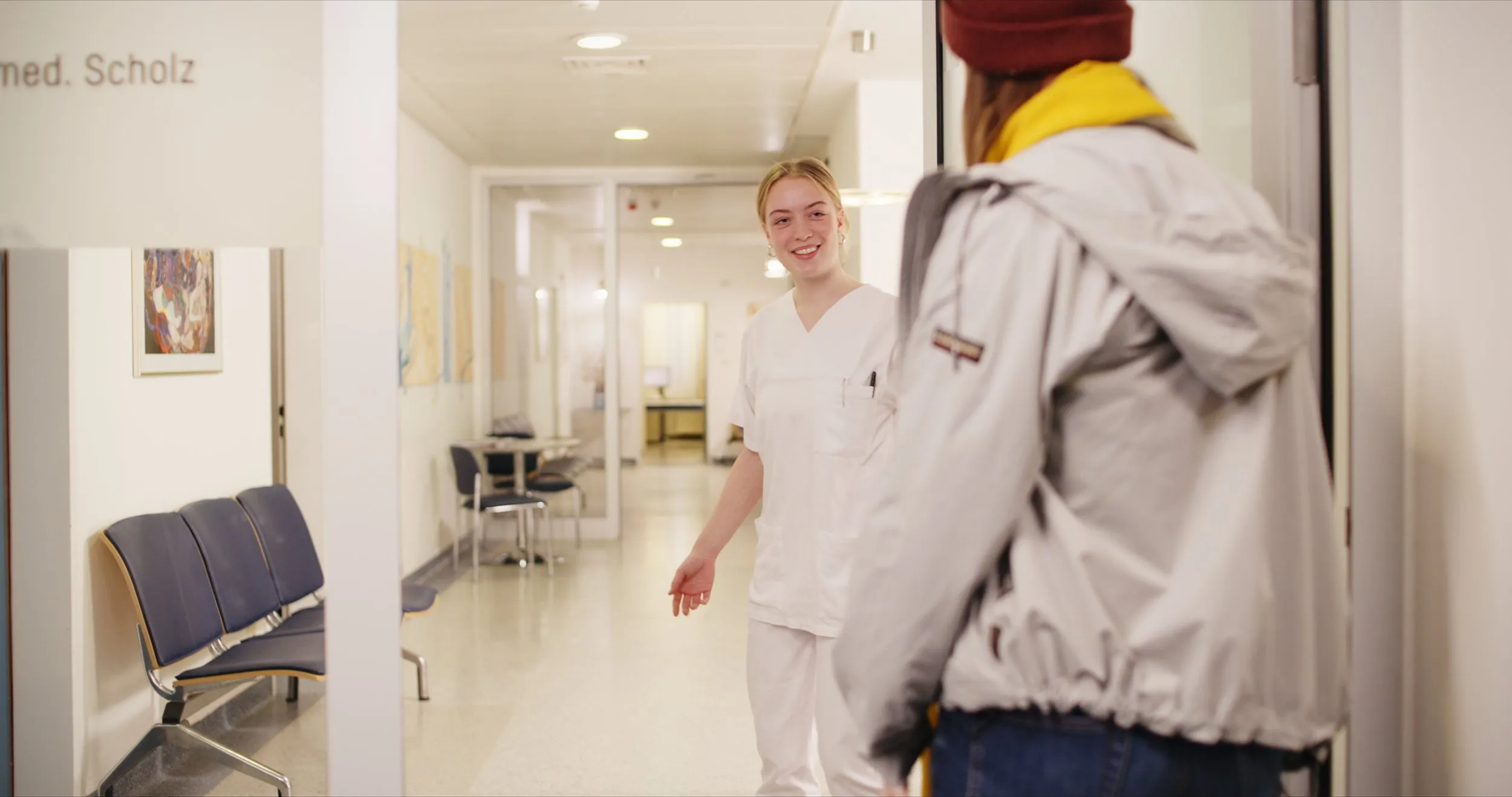 Pflegekraft begrüßt eine Patientin auf dem Klinikflur