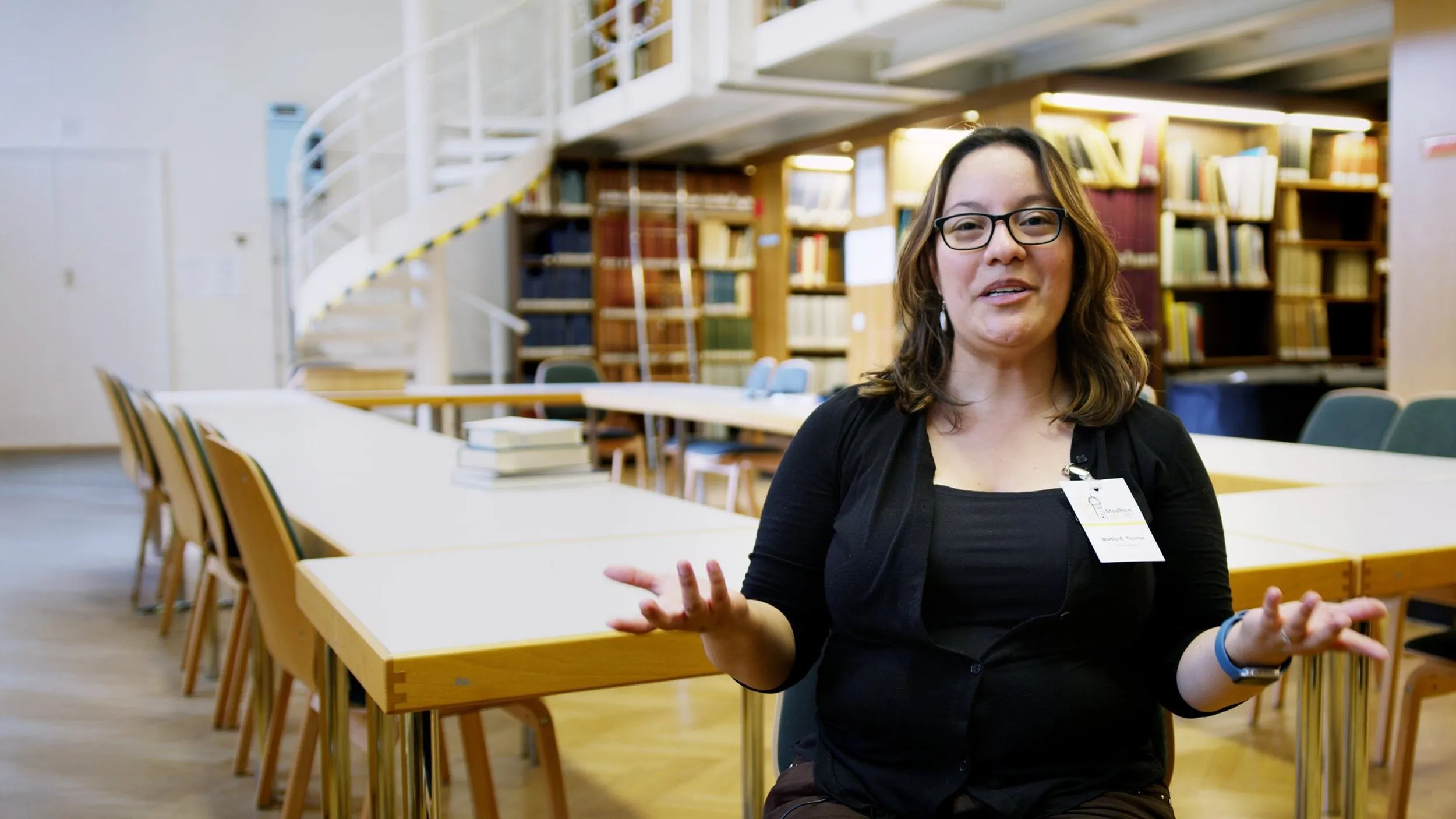 Wissenschaftlerin spricht in einer Bibliothek in die Kamera