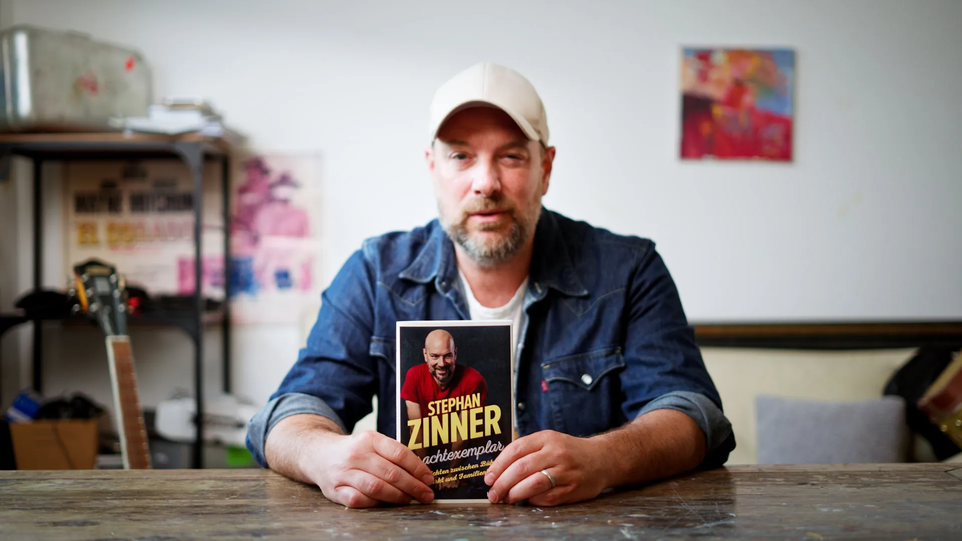 Stephan Zinner sitzt am Tisch und hält sein Buch „Prachtexemplar“ in die Kamera