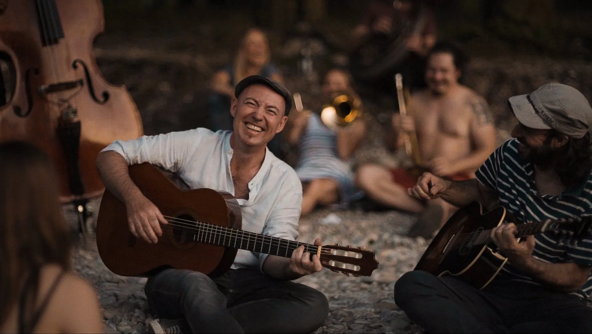 Lachender Musiker mit Gitarre sitzt abends mit anderen Musikern im Kreis
