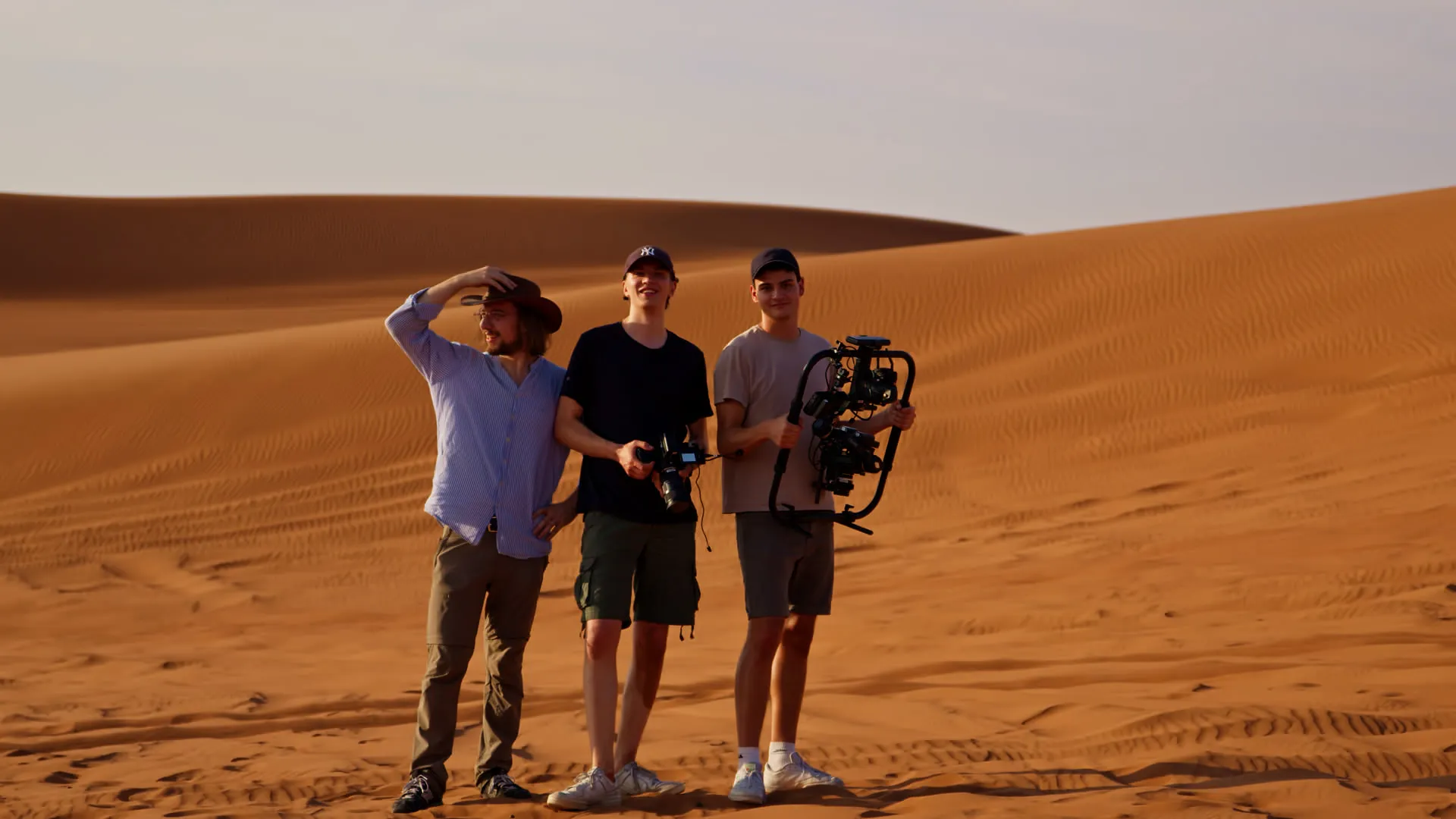 Drei Filmemacher mit Kamera und Gimbal stehen in einer Wüste mit orangefarbenen Sanddünen