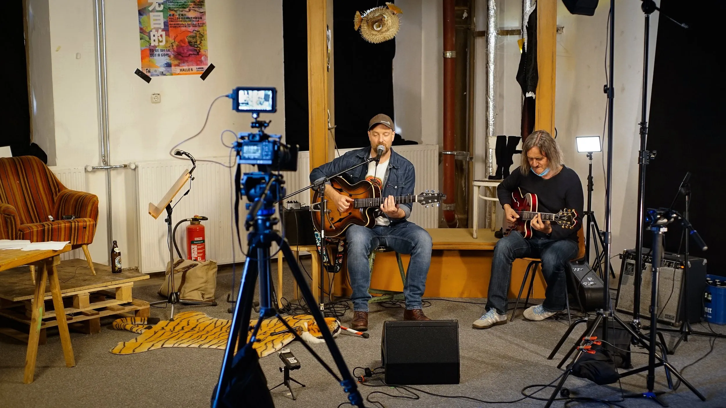 Zwei Musiker mit Gitarren auf einer kleinen Bühne, davor eine Kamera auf Stativ