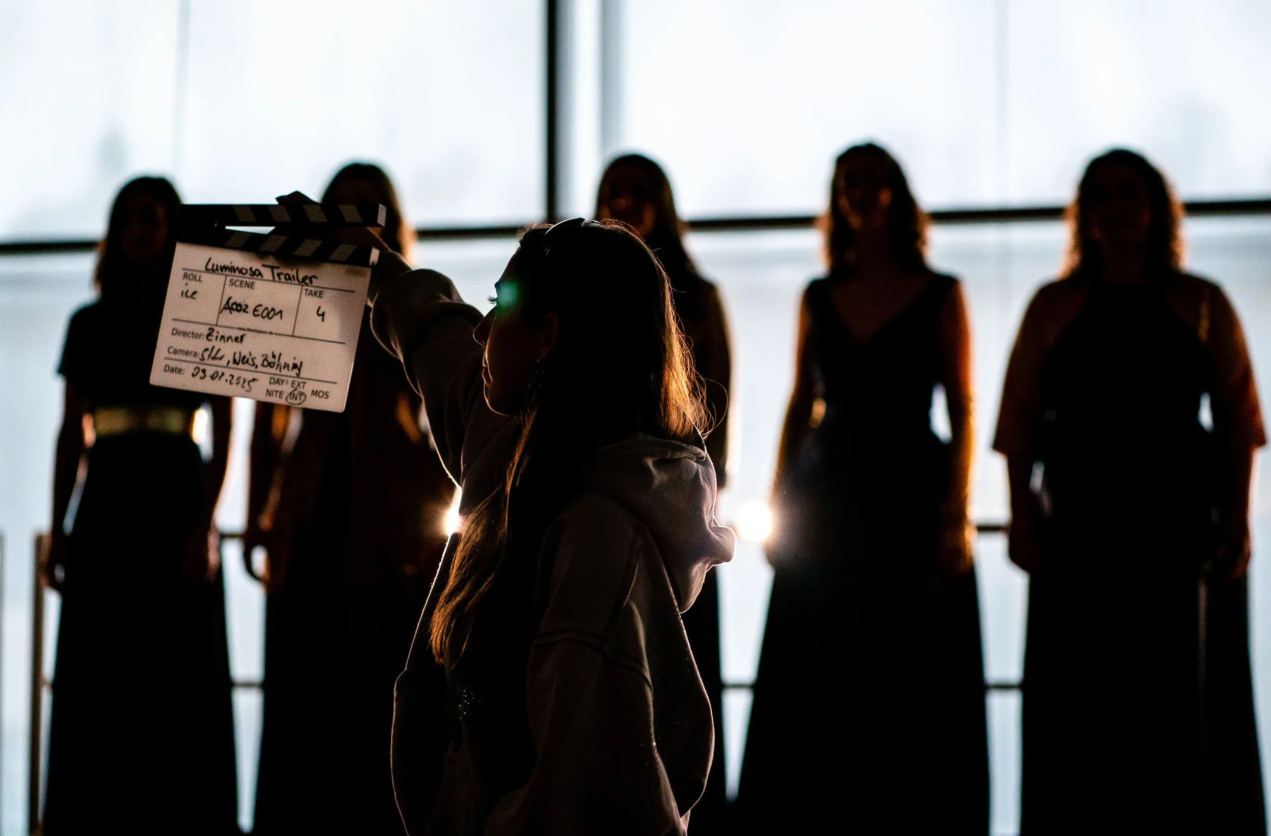 Darstellerin hält eine Filmklappe vor einer Gruppe im Gegenlicht
