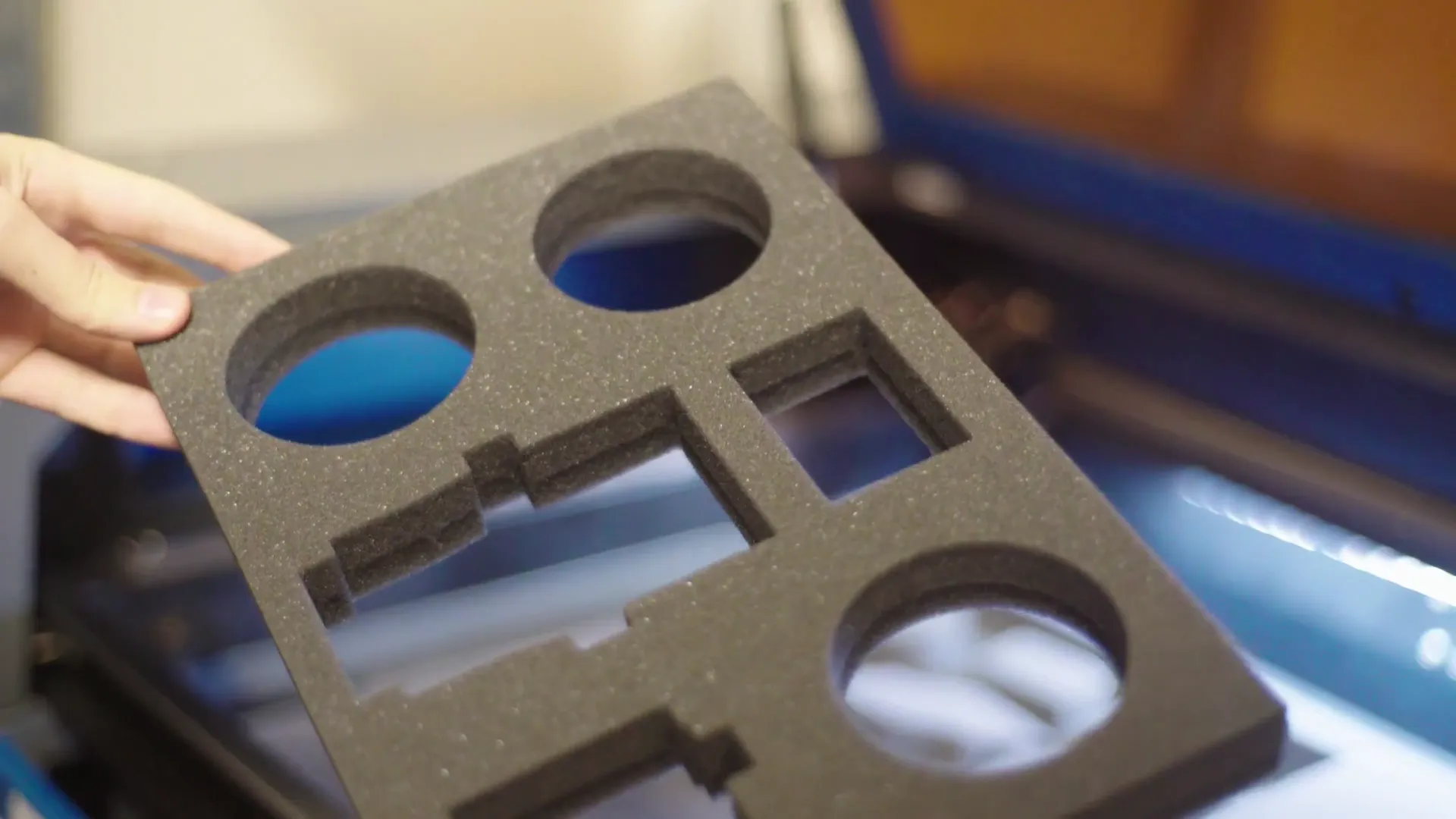 Frisch gelaserte Schaumstoffeinlage mit runden und eckigen Aussparungen wird aus dem Lasercutter gehoben